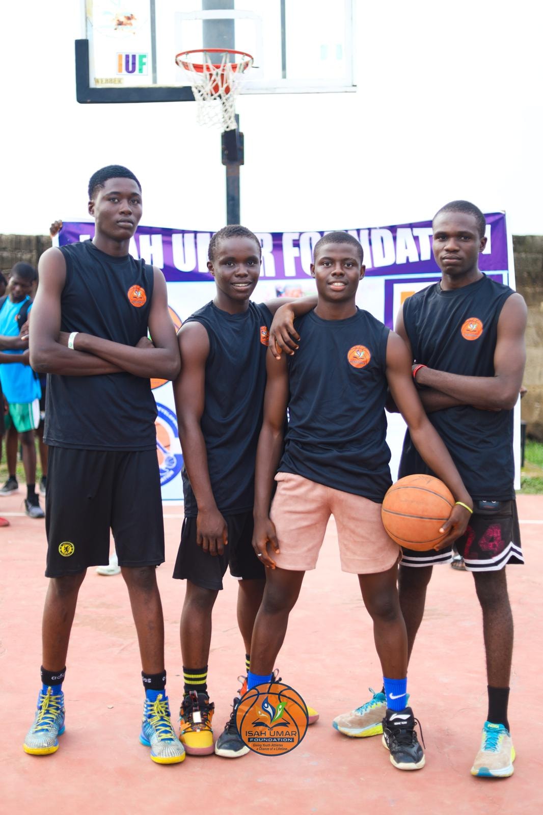 Four boys in black IUF jerseys posing together in front of the foundation banner