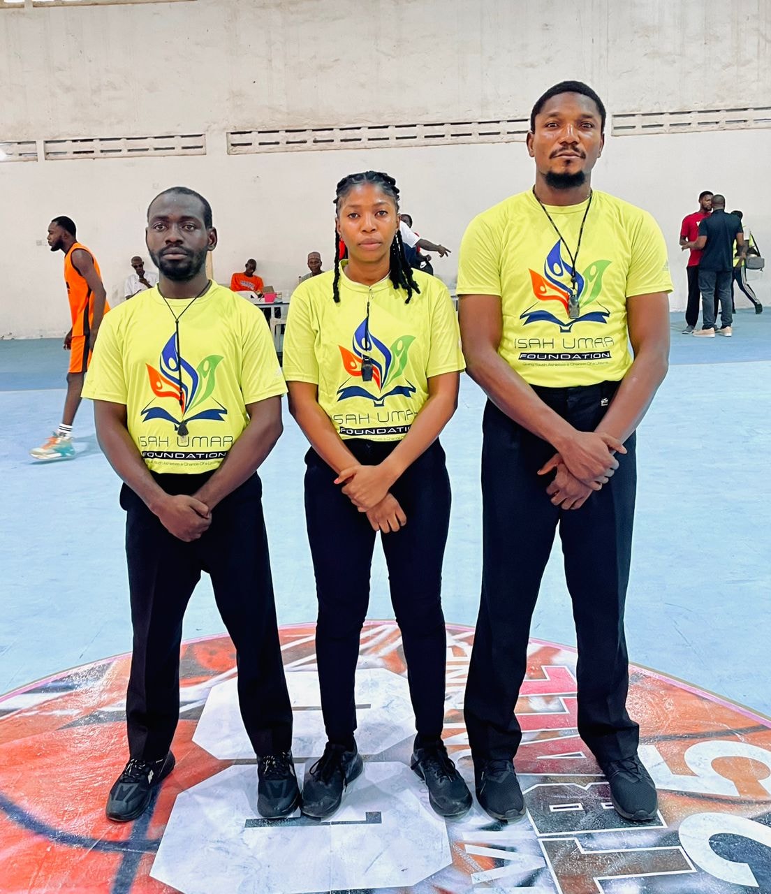 Three Isah Umar Foundation officials in yellow IUF shirts standing on court