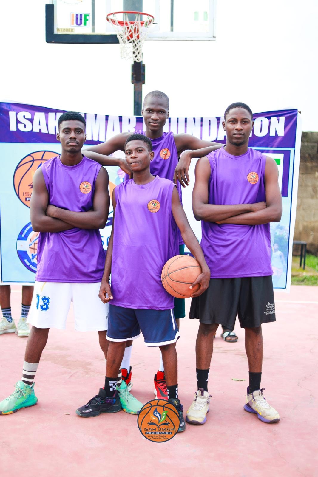Four boys in purple IUF jerseys posing in front of the Isah Umar Foundation banner